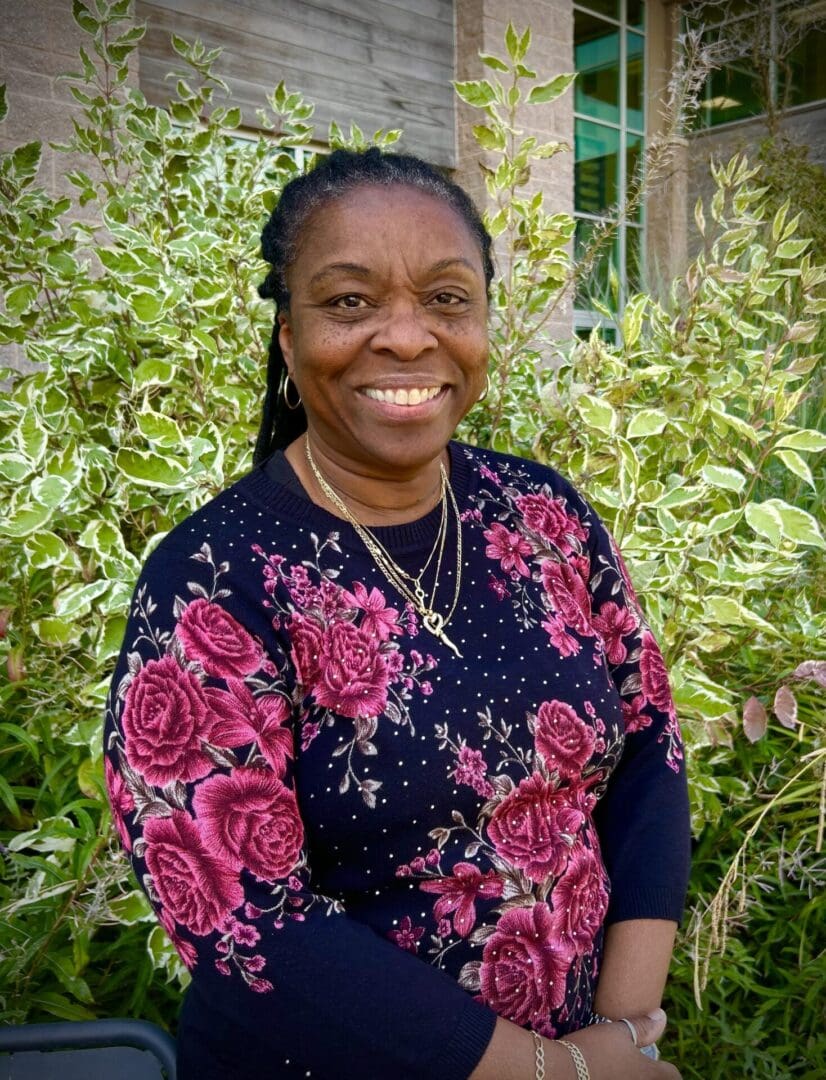 A woman standing in front of bushes and trees.