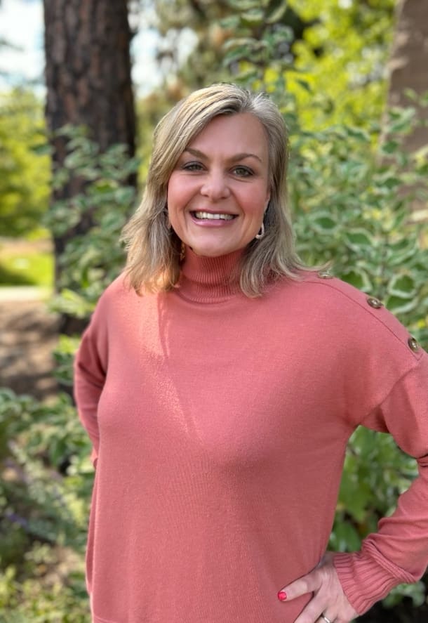 A woman in pink shirt standing next to trees.